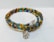 A vibrant beaded bracelet featuring small, round, glass beads in various colors including blue, orange, green, and yellow. There is a silver charm shaped like a hand with a star cutout, attached to the bracelet, which adds a decorative element.