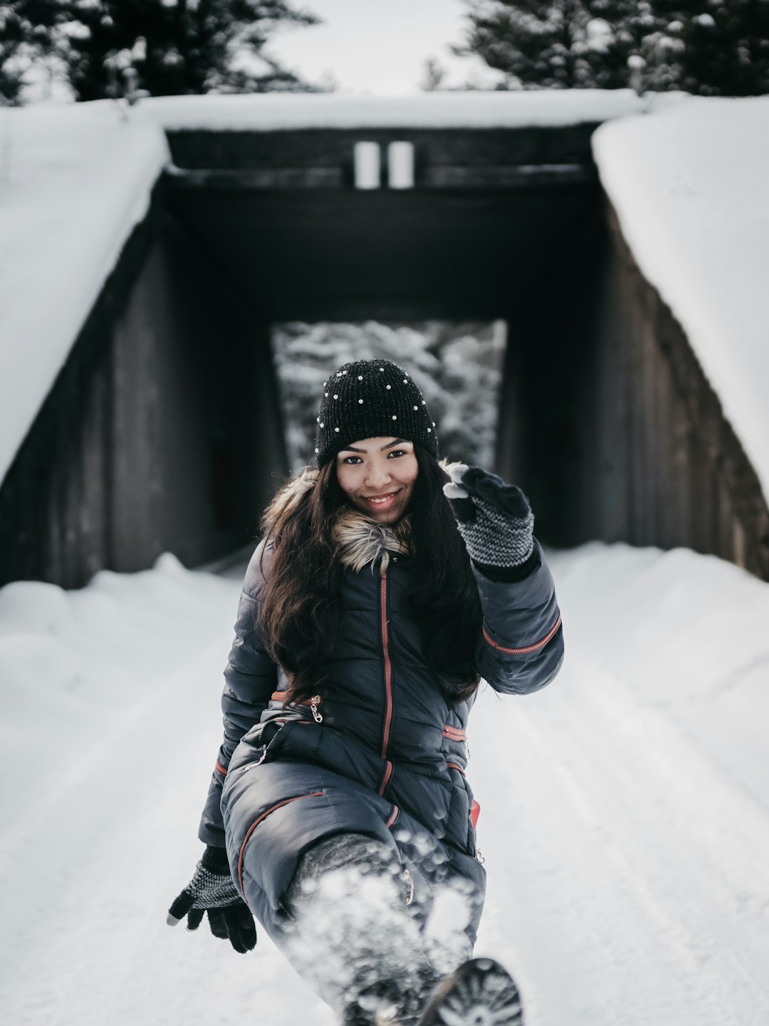 woman in black jacket and blue denim jeans sitting on snow covered ground during daytime