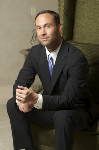 man in black suit jacket and black pants sitting on green sofa