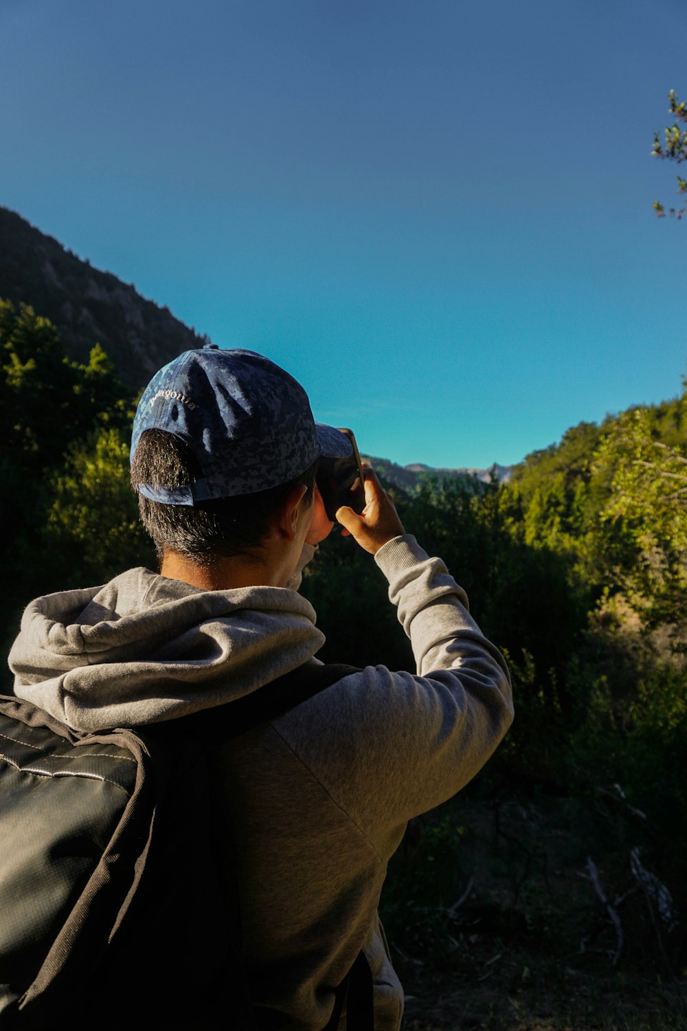 man in black jacket and black cap taking photo of green trees during daytime