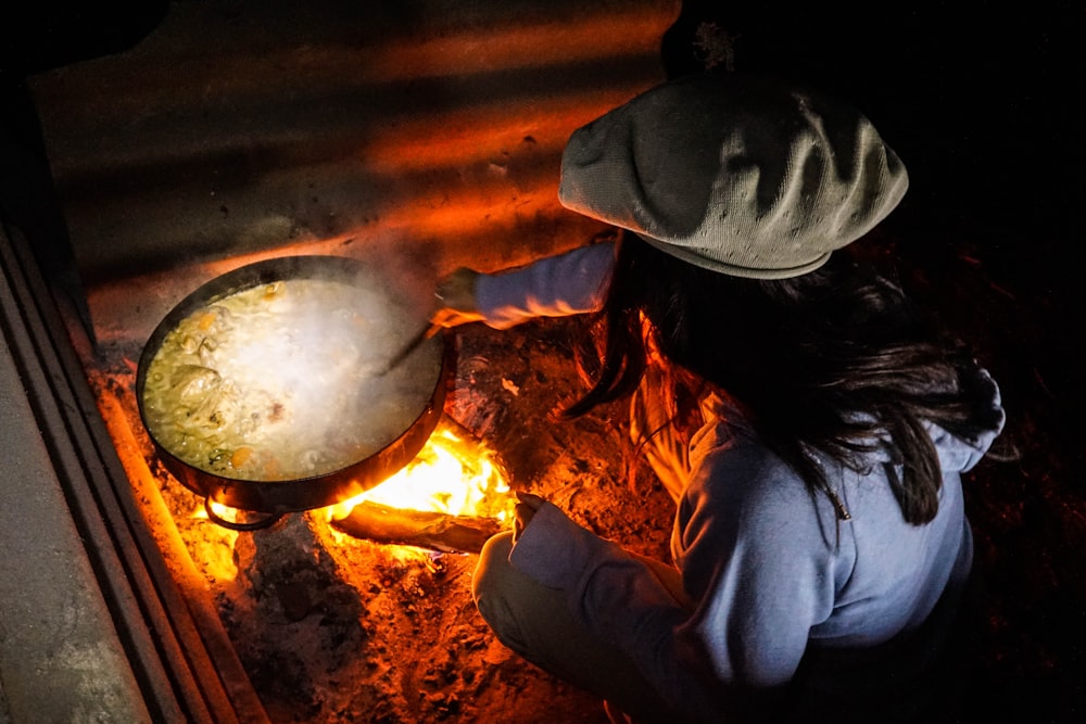 person in gray long sleeve shirt and black hat holding a stainless steel cooking pot