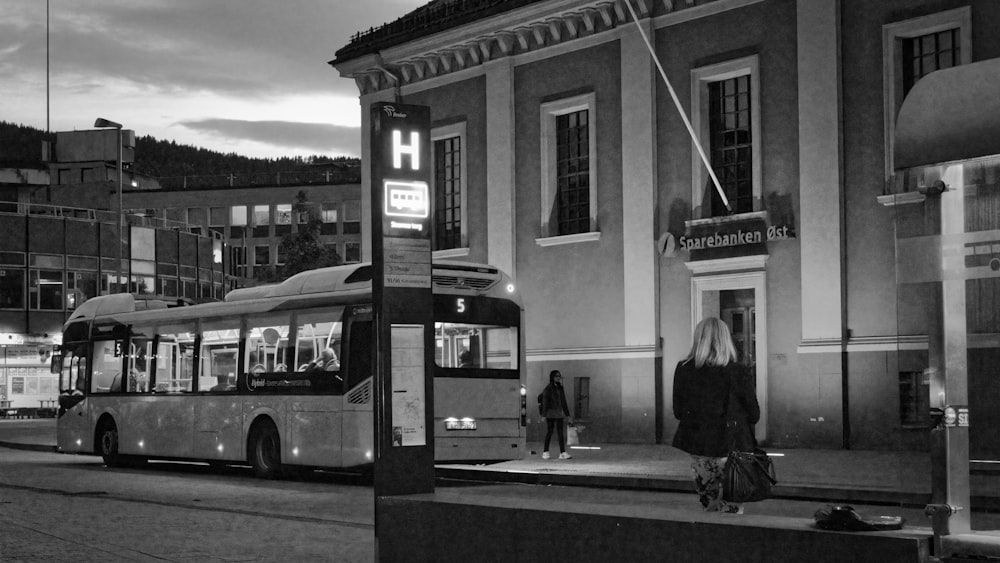grayscale photo of man in black jacket standing near bus