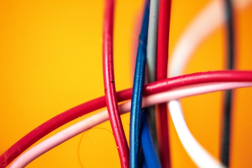 A close-up view of several intertwined colorful cables against a vibrant yellow background. The cables are primarily red, blue, and white, creating a dynamic and chaotic pattern.