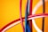 A close-up view of several intertwined colorful cables against a vibrant yellow background. The cables are primarily red, blue, and white, creating a dynamic and chaotic pattern.