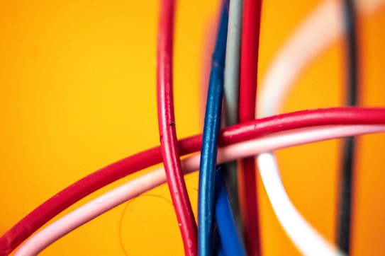 A close-up view of several intertwined colorful cables against a vibrant yellow background. The cables are primarily red, blue, and white, creating a dynamic and chaotic pattern.