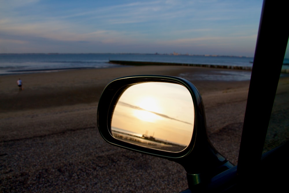 black car side mirror with a view of a gray field under blue sky during daytime