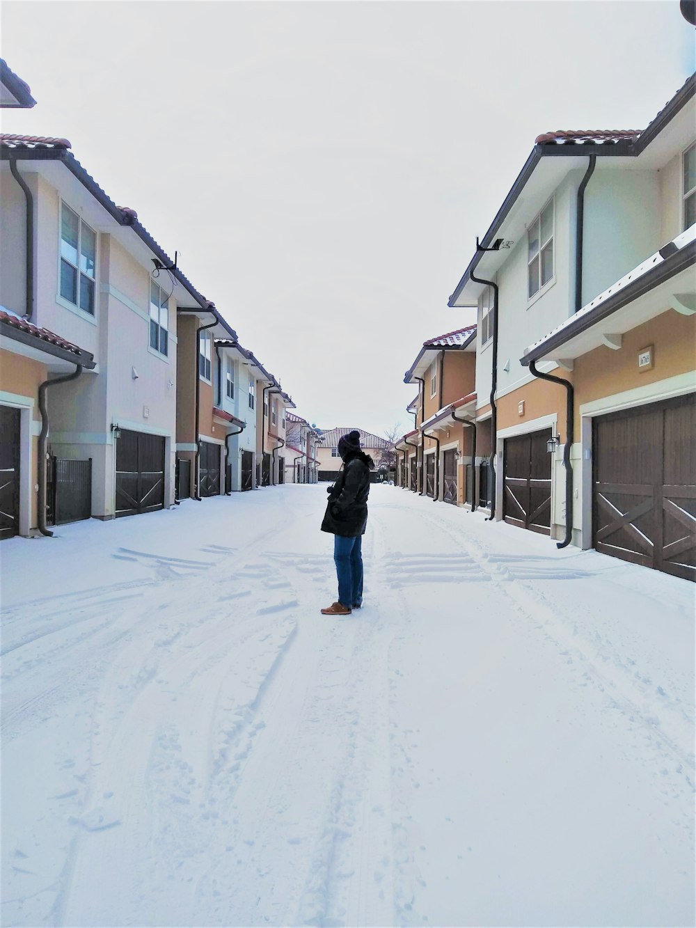 Donna in giacca nera che cammina sul sentiero coperto di neve tra le case durante il giorno