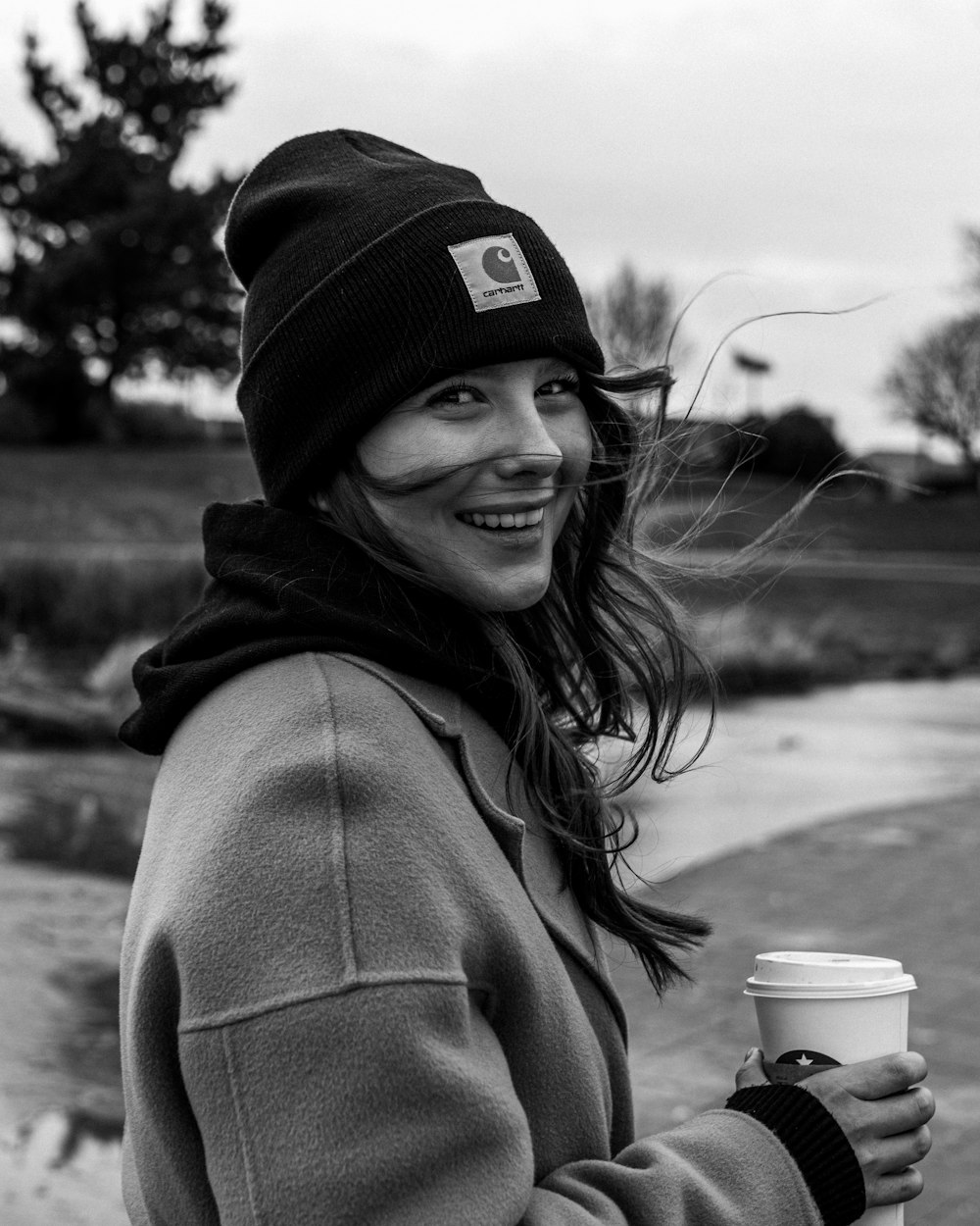 Photo en niveaux de gris d’une femme en manteau et bonnet en tricot souriant