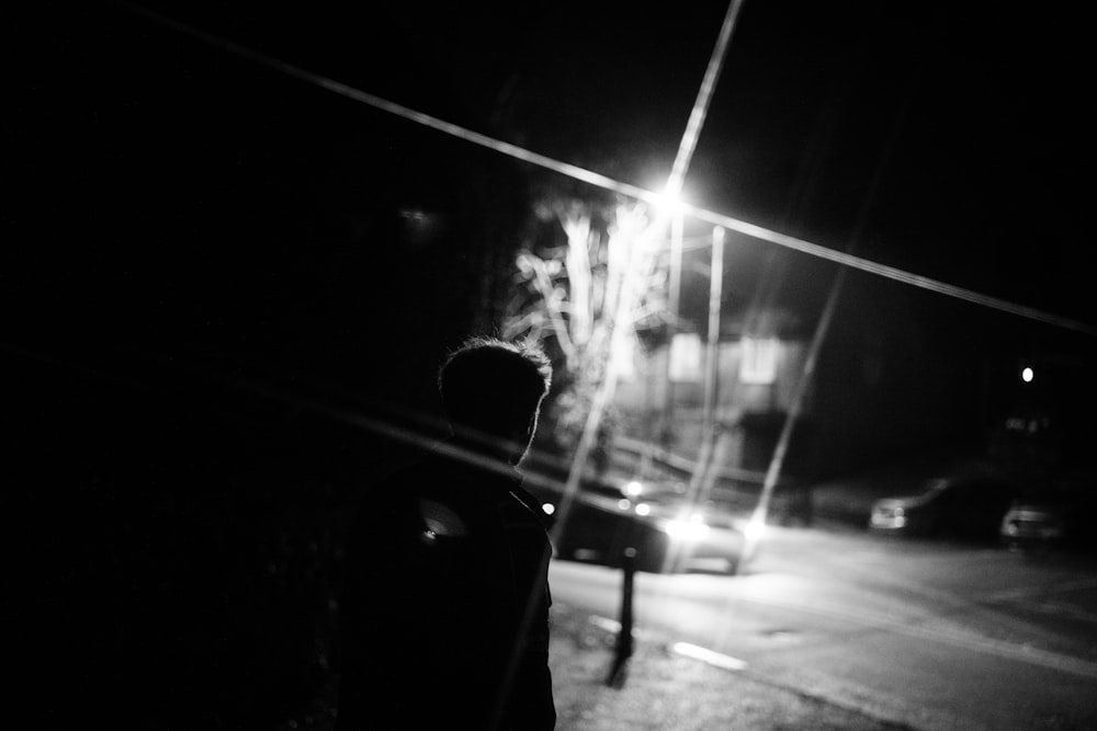 man in black jacket standing on sidewalk during night time