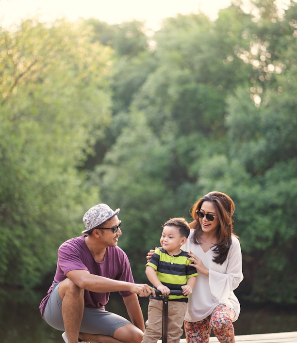 a man and a woman giving attention to a young child on a scooter