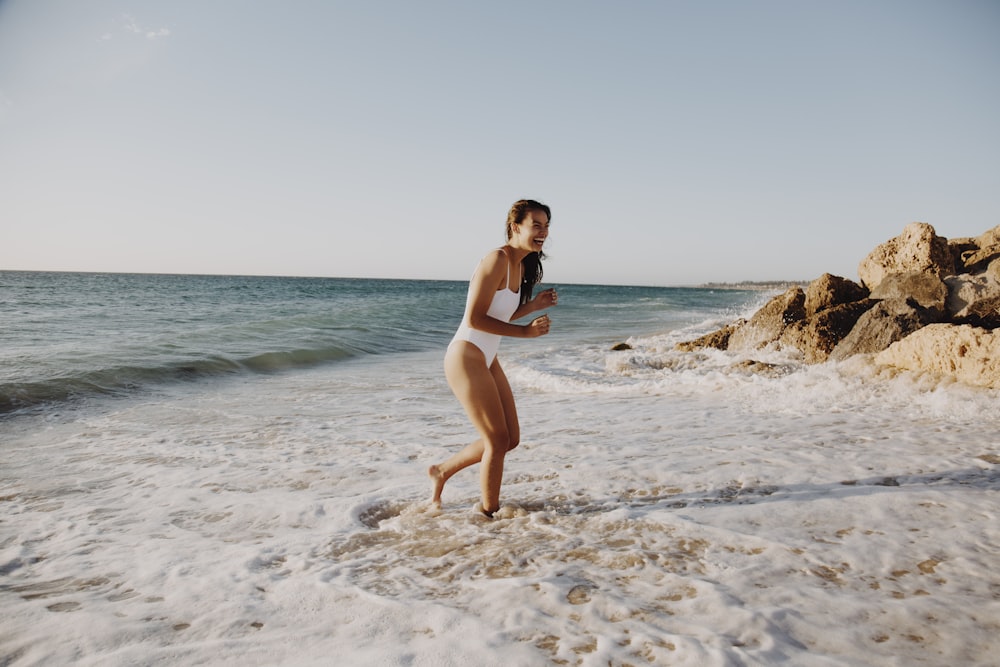 Frau im weißen Bikini steht tagsüber am Strand