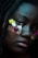 A close-up of a person with a nose ring and decorative bandages on their face. The bandages have flowers attached to them and display the words 'take care.' The lighting creates a moody, atmospheric effect, highlighting the person's expressive eyes and lips.