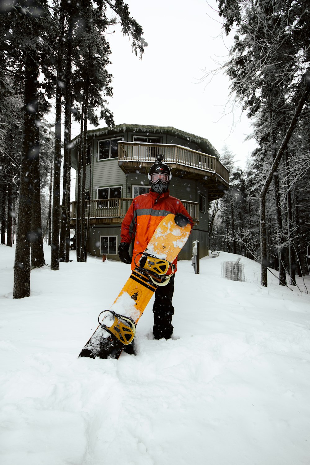 Hombre en chaqueta naranja y pantalones negros montando en una tabla de snowboard amarilla en suelo cubierto de nieve durante