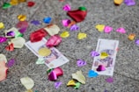 Colorful confetti, rose petals, and two 500 denomination currency notes scattered on a gray stone surface.