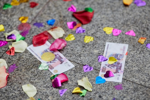 Colorful confetti, rose petals, and two 500 denomination currency notes scattered on a gray stone surface.