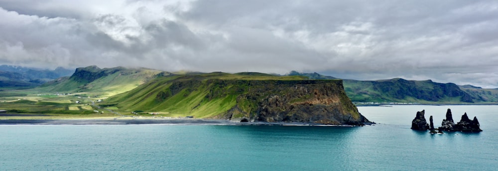 green and brown mountain beside blue sea under white clouds and blue sky during daytime