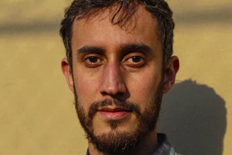 A close-up of a well-groomed man with a full beard, natural light highlighting his confident expression.