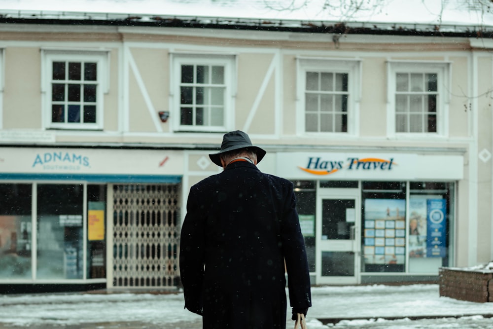 Hombre con abrigo negro caminando sobre suelo cubierto de nieve durante el día