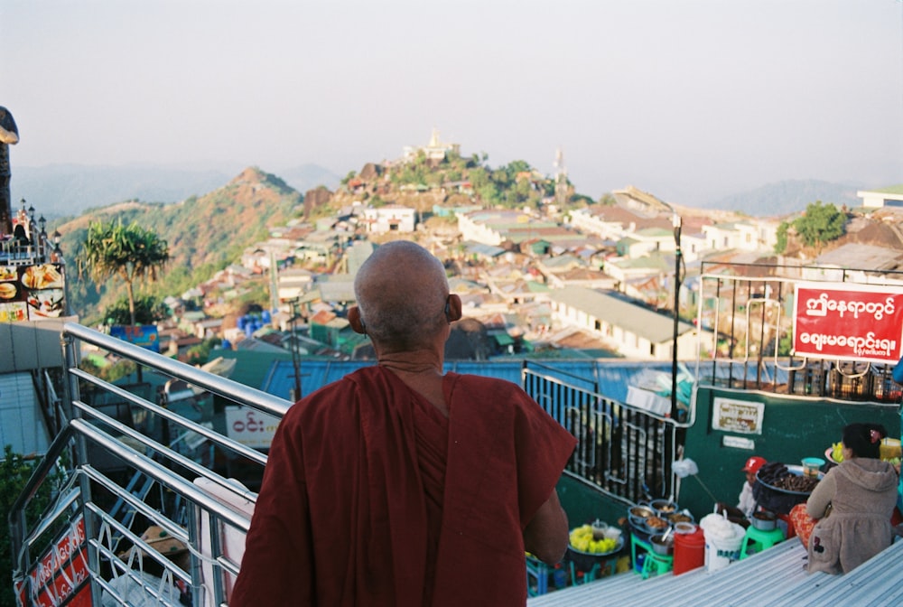 man in red shirt standing on top of building looking at the city during daytime