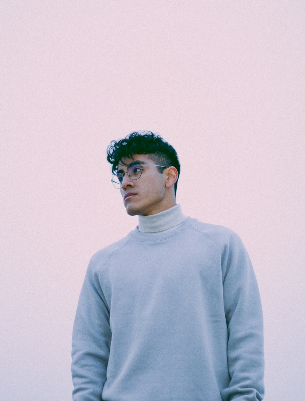 a man with glasses standing in front of a white wall