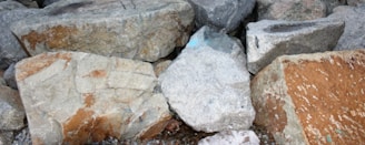 Several large, rough stones of varying sizes and colors are piled together. The stones have an uneven texture and display natural patterns and colors, including shades of gray, brown, and hints of blue.
