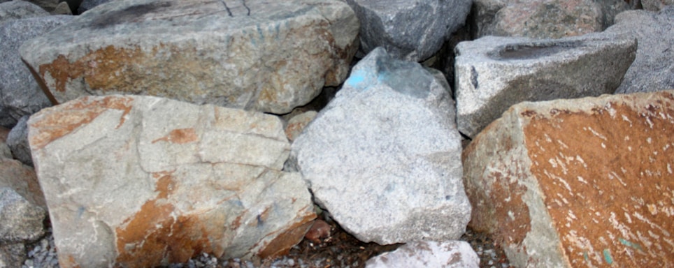 Several large, rough stones of varying sizes and colors are piled together. The stones have an uneven texture and display natural patterns and colors, including shades of gray, brown, and hints of blue.