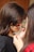A young girl is having her face painted with black and orange stripes by another person. The focus is on the artistic application of the paint, capturing a close-up view of the hands and brush. The girl's hair is long and brown, and she is wearing a black top.