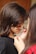 A young girl is having her face painted with black and orange stripes by another person. The focus is on the artistic application of the paint, capturing a close-up view of the hands and brush. The girl's hair is long and brown, and she is wearing a black top.