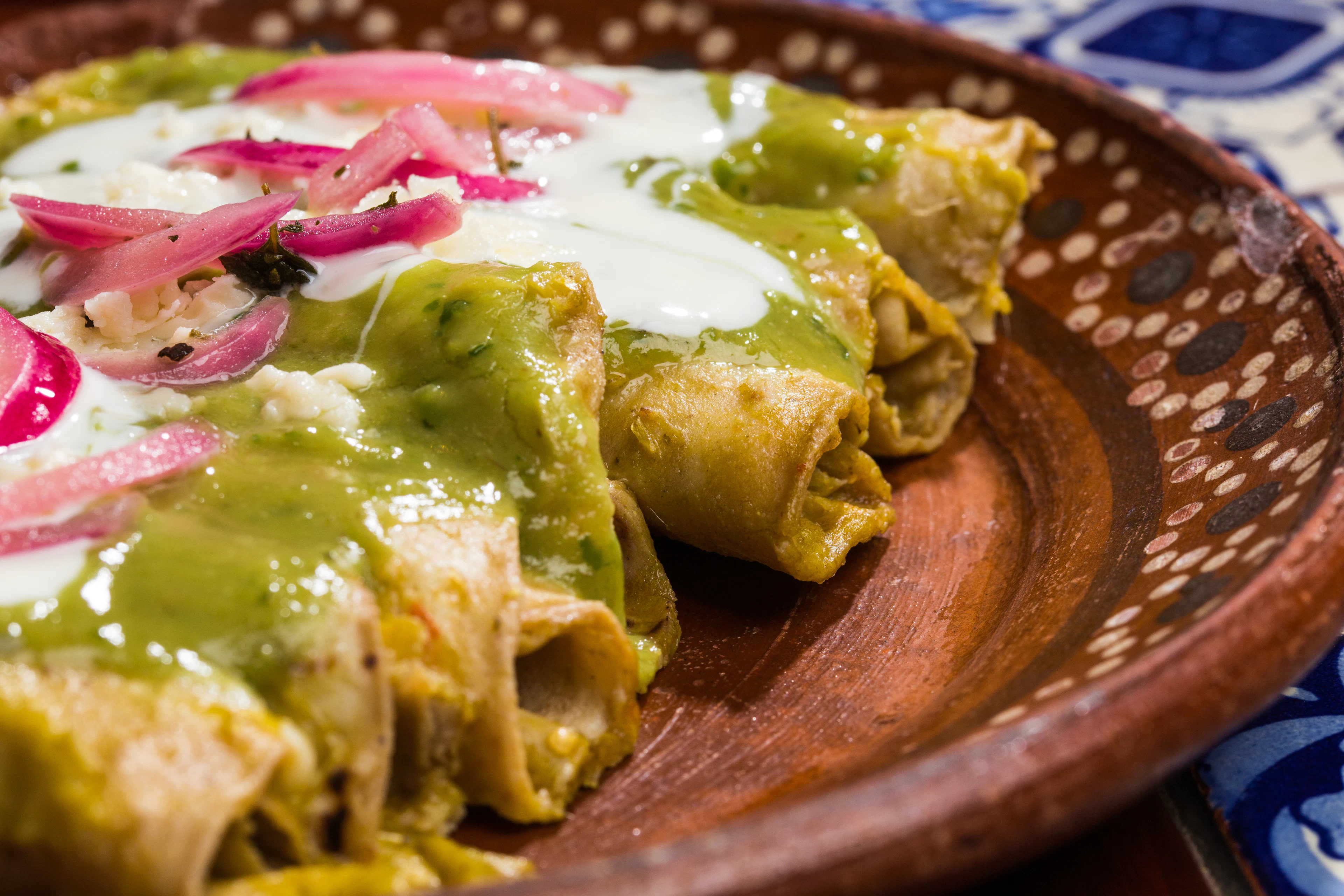Chicken enchiladas covered in green salsa with crema and pink pickled onions
