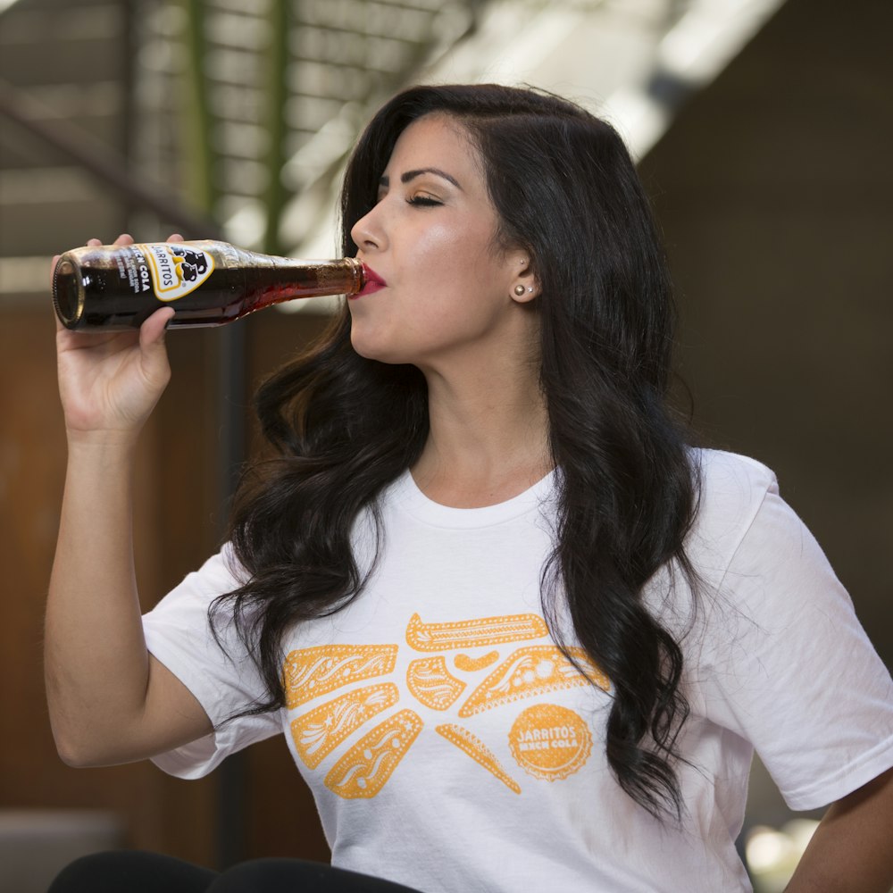 woman in white and orange crew neck t-shirt drinking coca cola