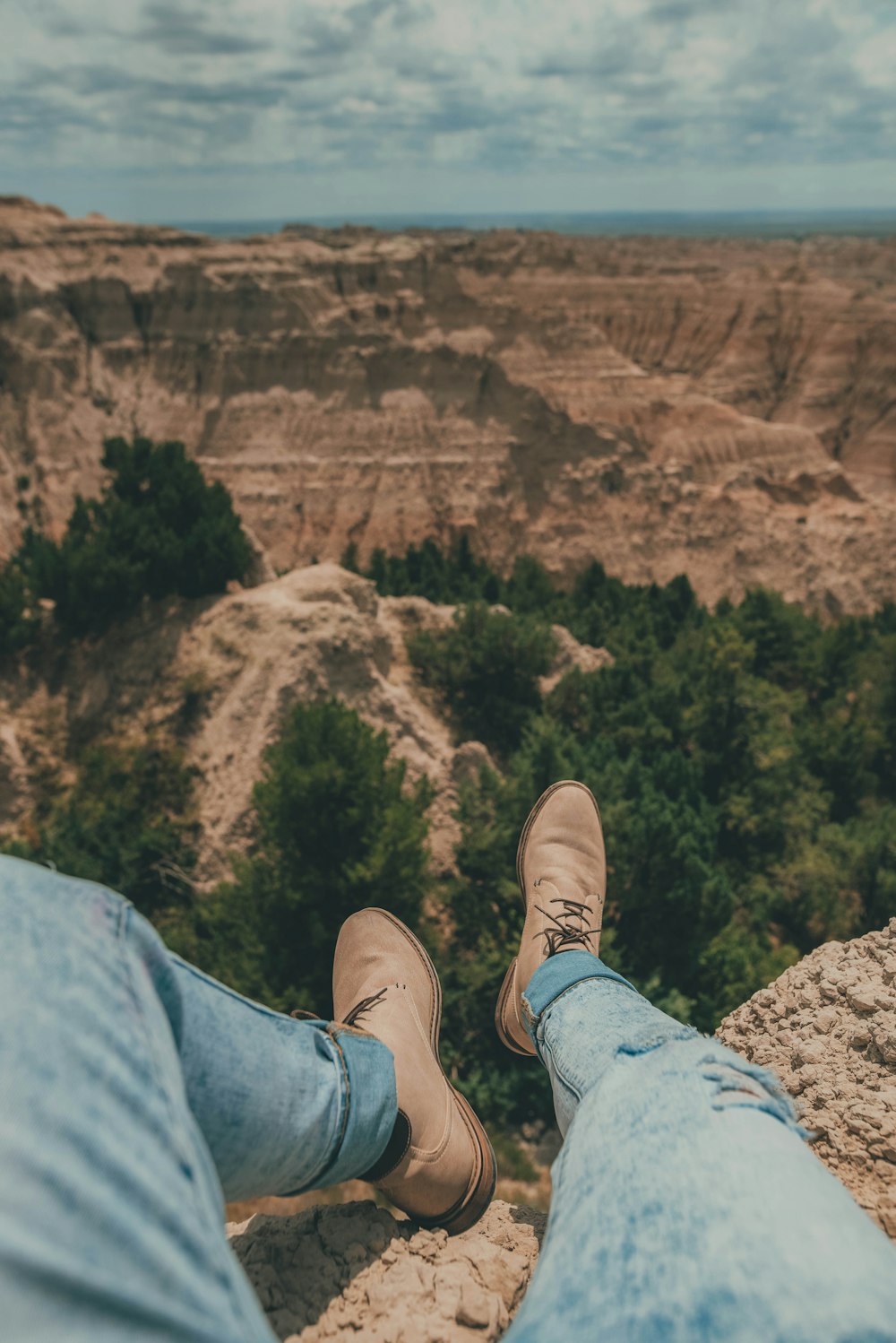 person in blue denim jeans and brown shoes sitting on rock formation during daytime