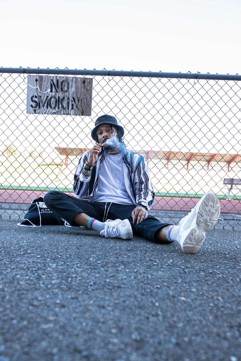 man in black jacket and blue denim jeans sitting on concrete pavement