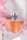 A clear glass perfume bottle with an orange-colored liquid inside is topped with a sleek silver cap and decorated with a delicate dark ribbon. The background is adorned with soft pink and white drapery, enhancing the luxurious and elegant feel.