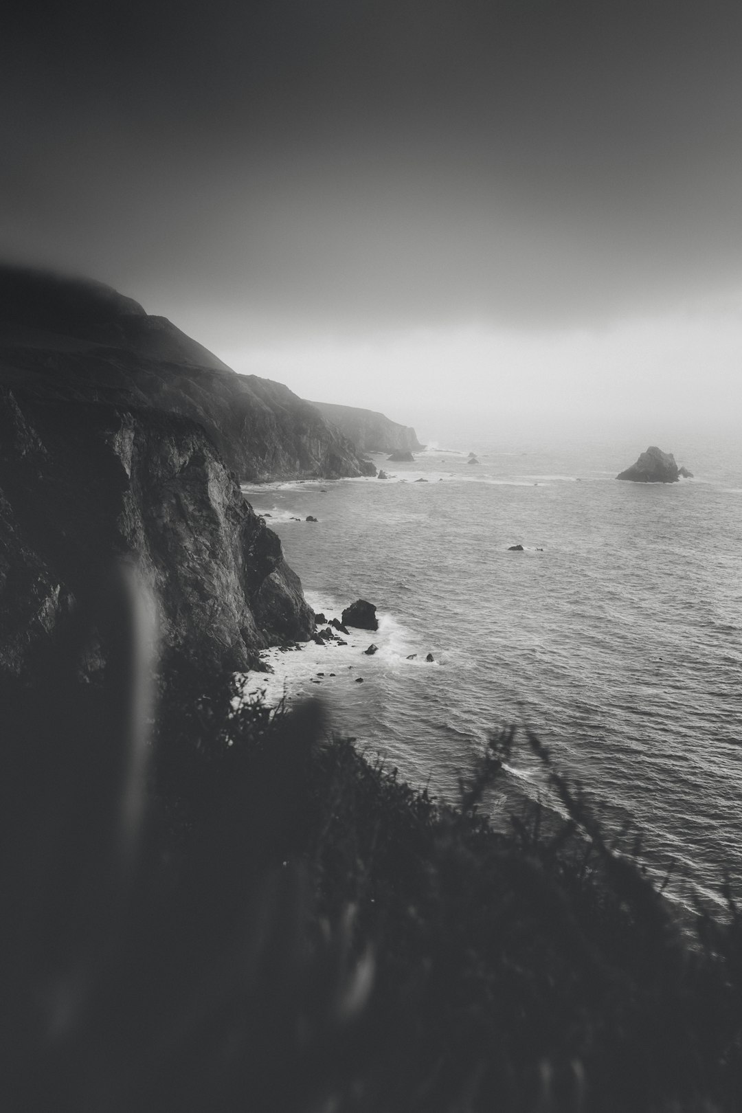 grayscale photo of sea waves crashing on rock formation