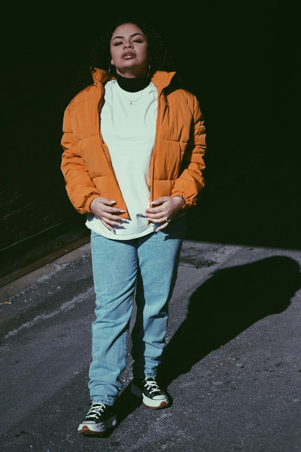 man in yellow jacket and blue denim jeans standing on road during nighttime