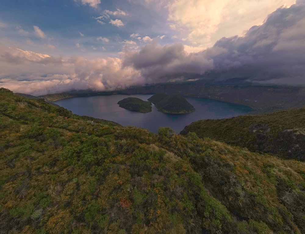 aerial view of lake between green mountains under cloudy sky during daytime