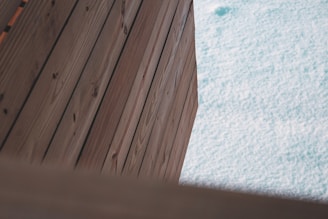 Wooden planks are arranged diagonally next to a light blue textured surface that resembles water. The wood grain is visible and the planks have a natural brown color.