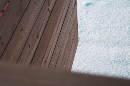 Wooden planks are arranged diagonally next to a light blue textured surface that resembles water. The wood grain is visible and the planks have a natural brown color.