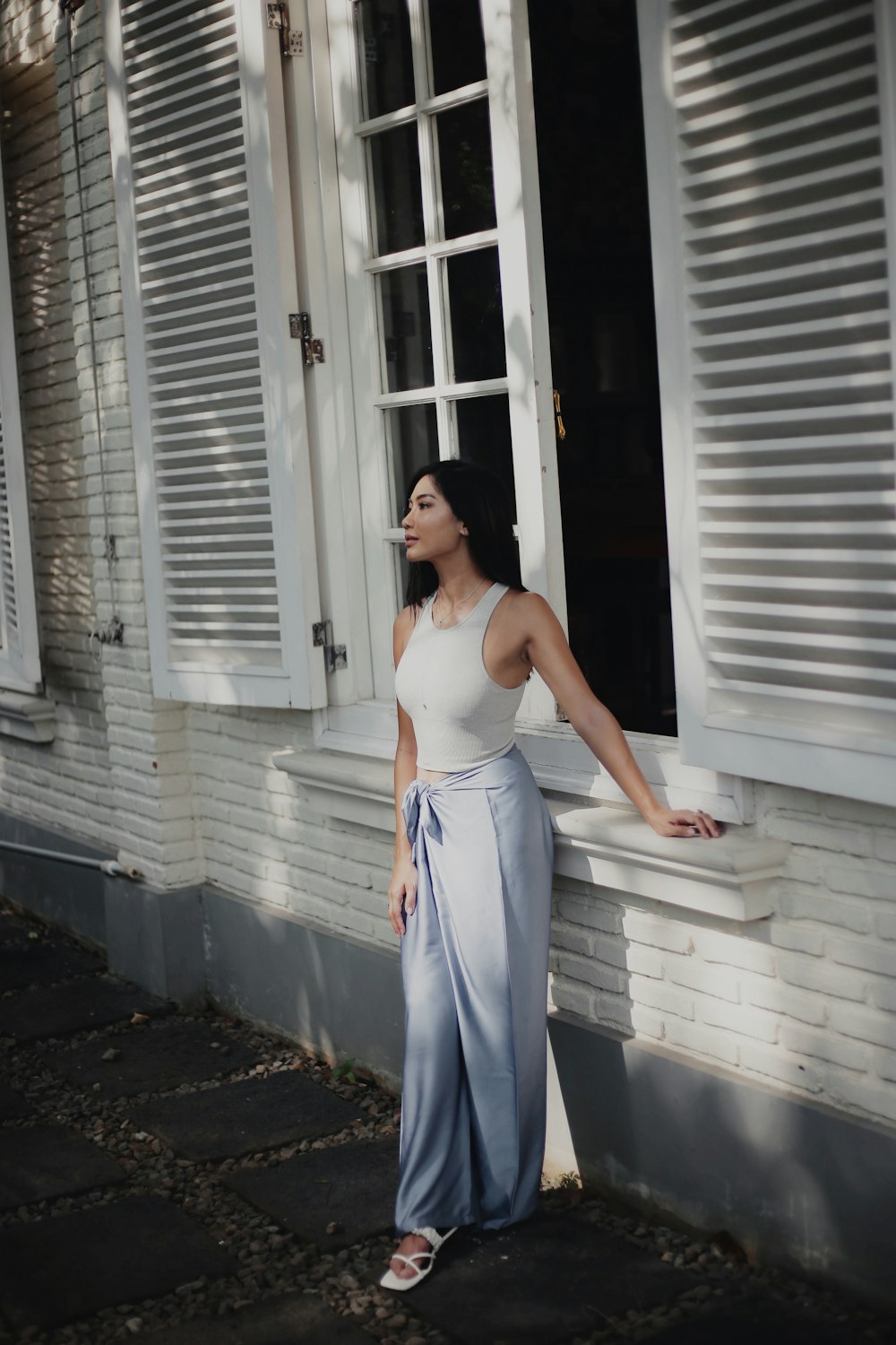woman in white tank top and blue pants standing in front of white wooden house during
