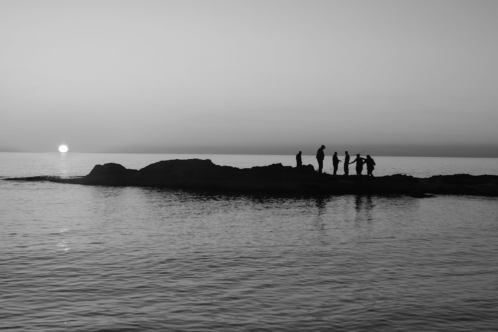 Silhouette von Menschen auf einer Felsformation mitten im Meer tagsüber
