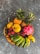 A vibrant arrangement of tropical fruits including bananas, pineapples, rambutan, dragon fruit, and a soursop, displayed in a wicker basket on a textured dark surface.