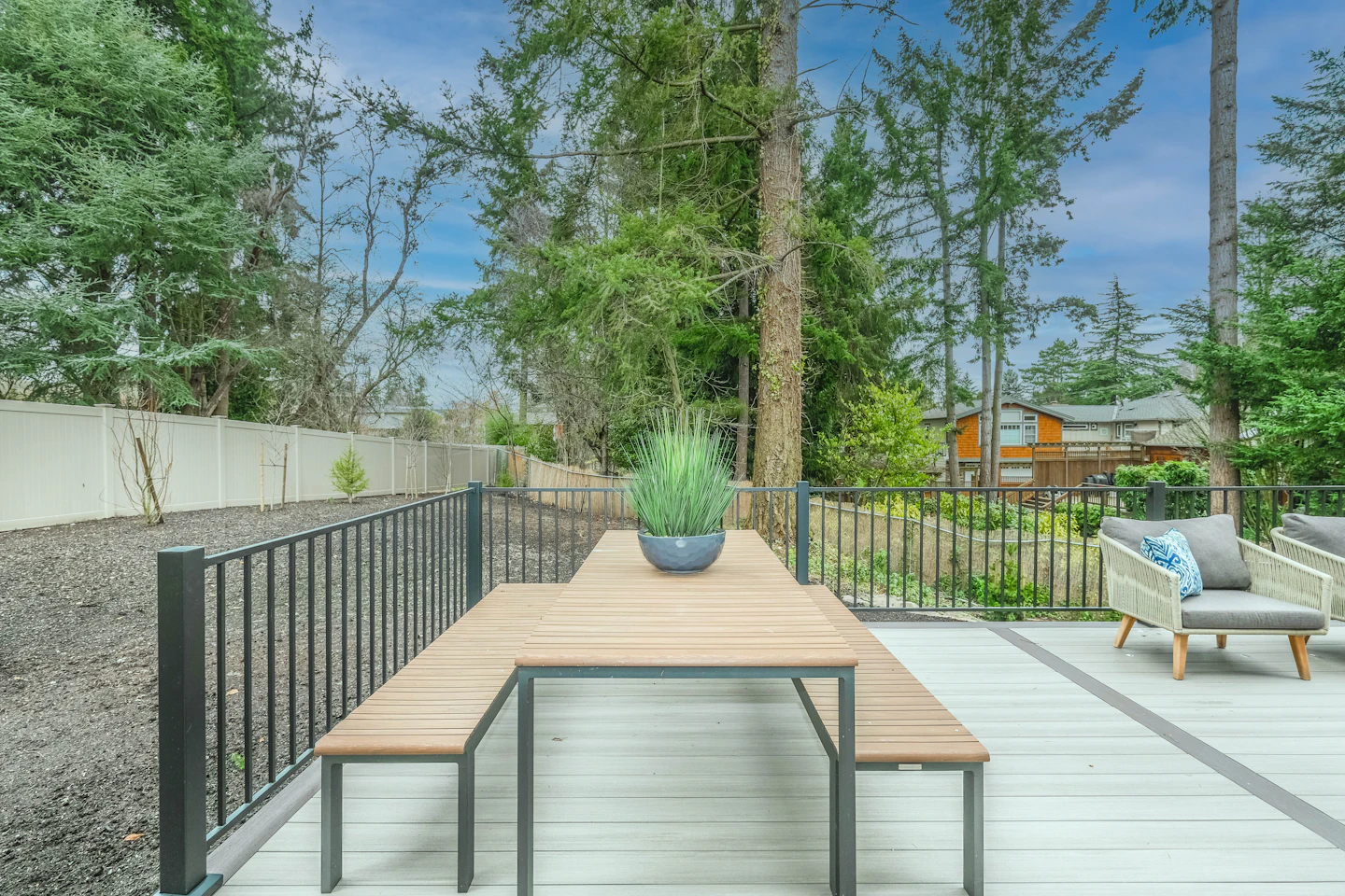 Deck dining area with a potted plant on the table and woods beyond the railing
