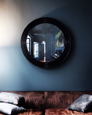 A cozy living room wall adorned with a large decorative round mirror reflecting soft natural light.