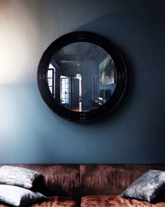 A cozy living room wall adorned with a large decorative round mirror reflecting soft natural light.