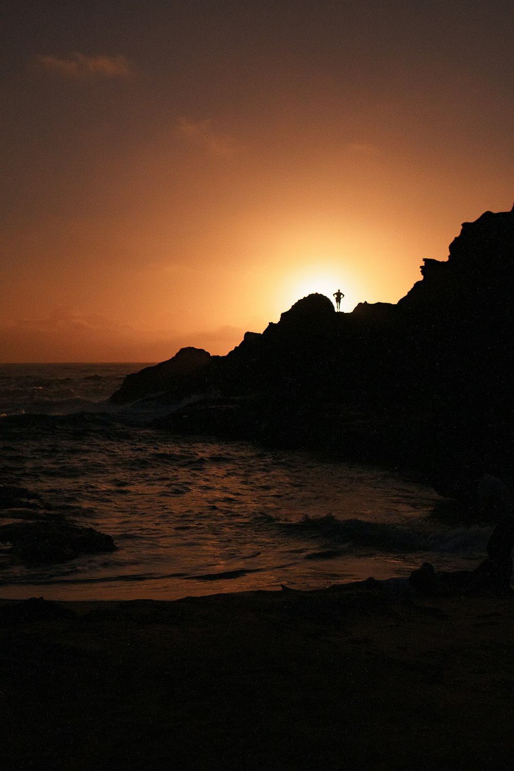 silhouette of rock formation on sea during sunset