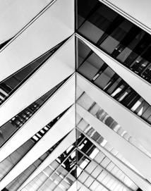 An abstract architectural pattern featuring a symmetrical design with diagonal lines composed of glass and reflective surfaces. The image displays a combination of geometric shapes and sharp angles, creating a sense of depth and perspective.