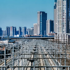 A cityscape with numerous high-rise buildings in the background, featuring a network of elevated train tracks and electrical lines. The scene captures a modern urban environment, focusing on infrastructure and dense development.