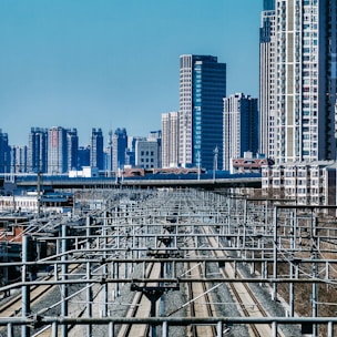 A cityscape with numerous high-rise buildings in the background, featuring a network of elevated train tracks and electrical lines. The scene captures a modern urban environment, focusing on infrastructure and dense development.