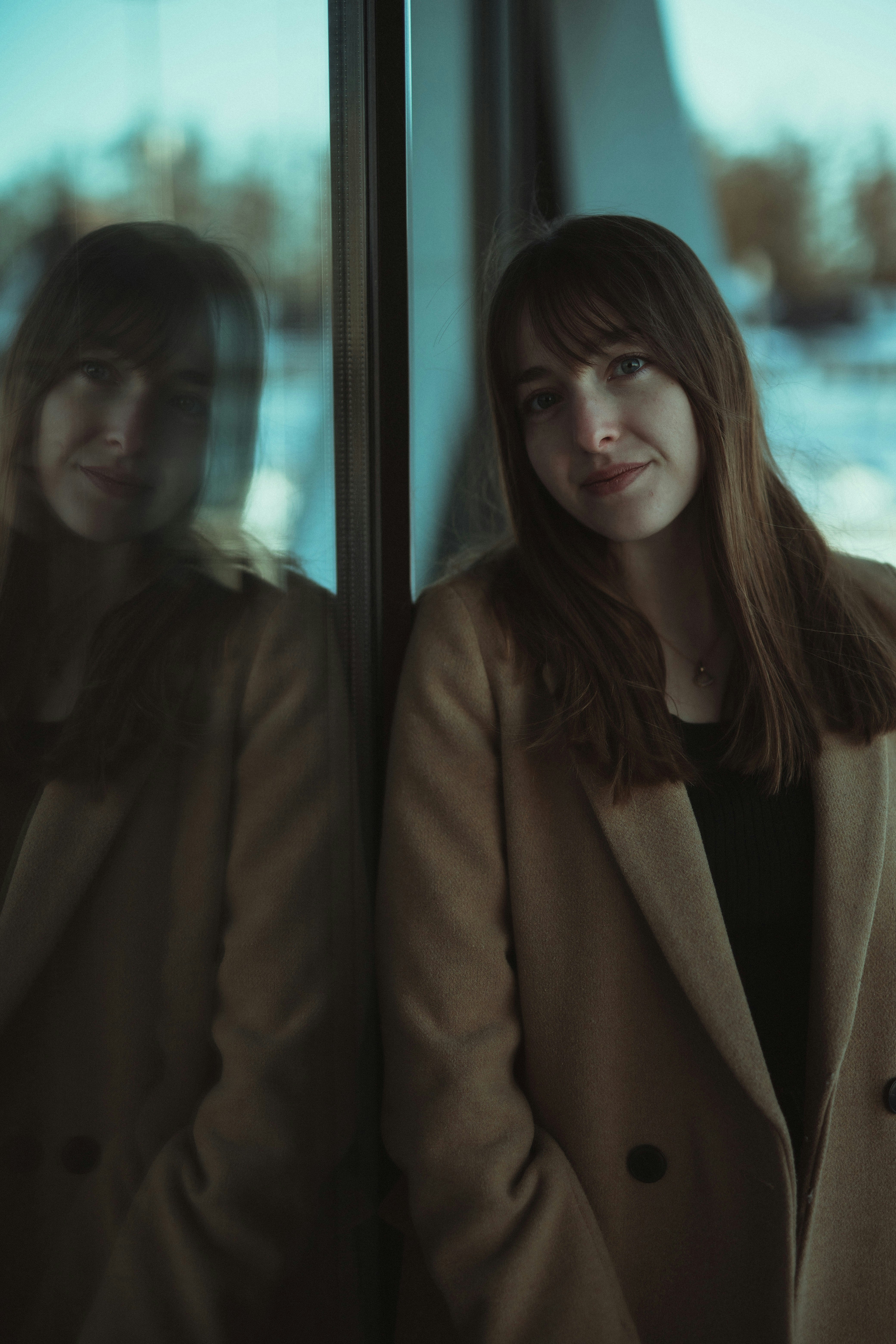 woman in brown coat standing beside glass window