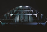 A tall structure with glass railings and visible metallic beams is illuminated by a series of lights, creating a modern and architectural appearance. The perspective gives a sense of looking up, highlighting the sleek design and symmetry of the structure against a dark background.